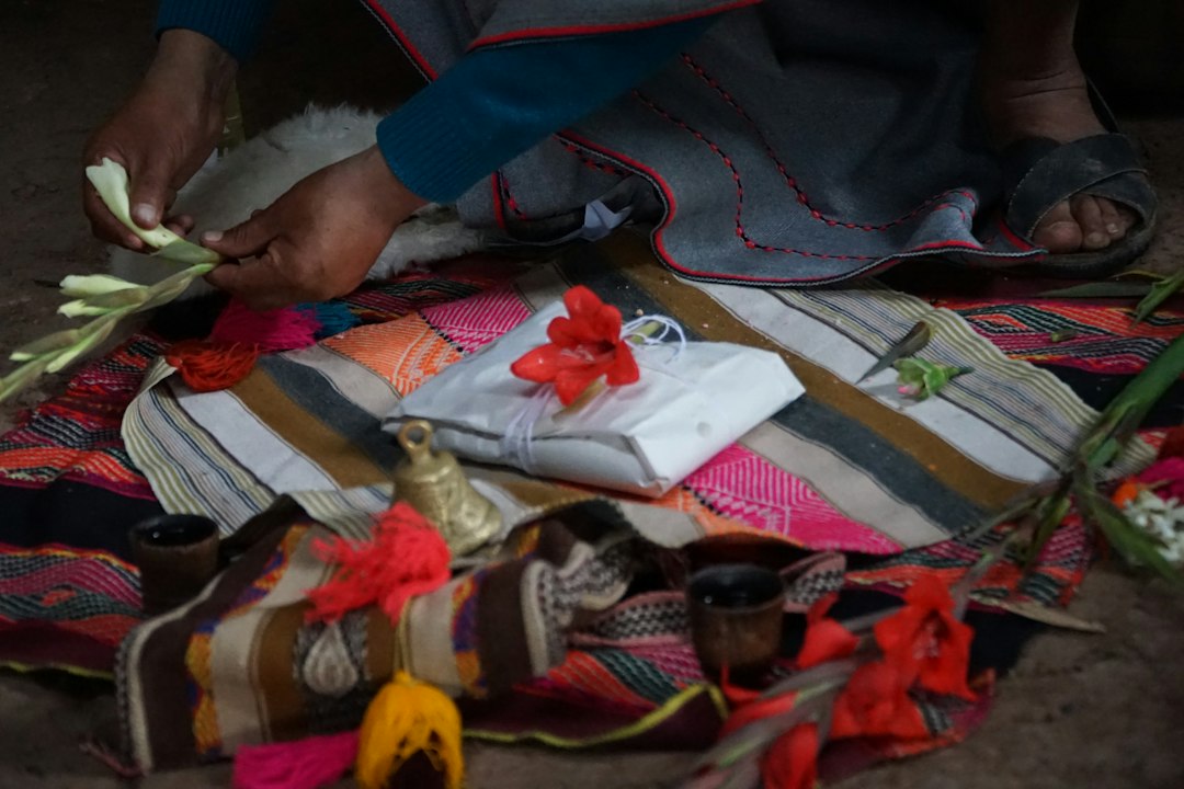 A person arranges offerings on a colorful woven cloth