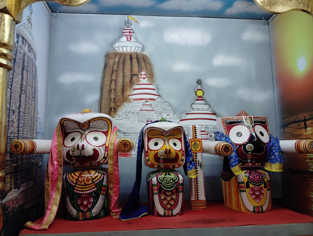 Three colorful wooden deities of Jagannath, Balabhadra, and Subhadra before a temple backdrop